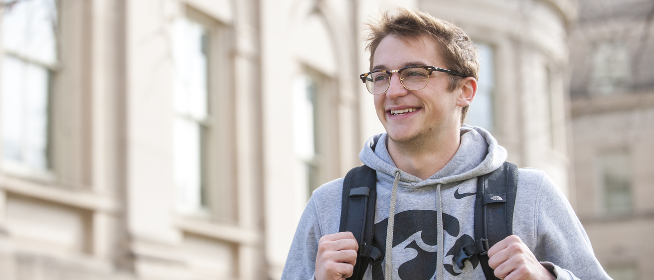 Male student with Hawkeye sweatshirt and backpack walking outside Schaeffer Hall