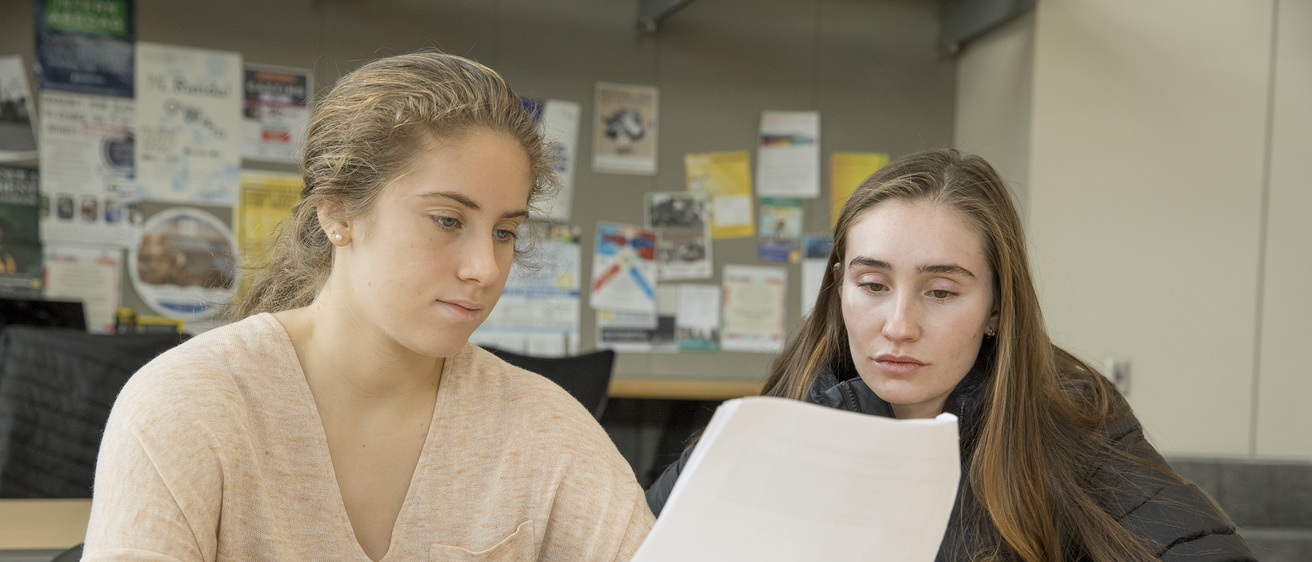 Two students working together at a table looking at a paper
